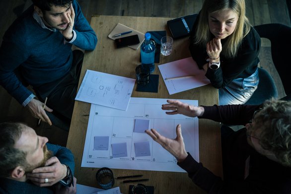 Blick von oben: Vier Menschen sitzen an einem Tisch und diskutieren über Unterlagen, die vor ihnen auf dem Tisch liegen.