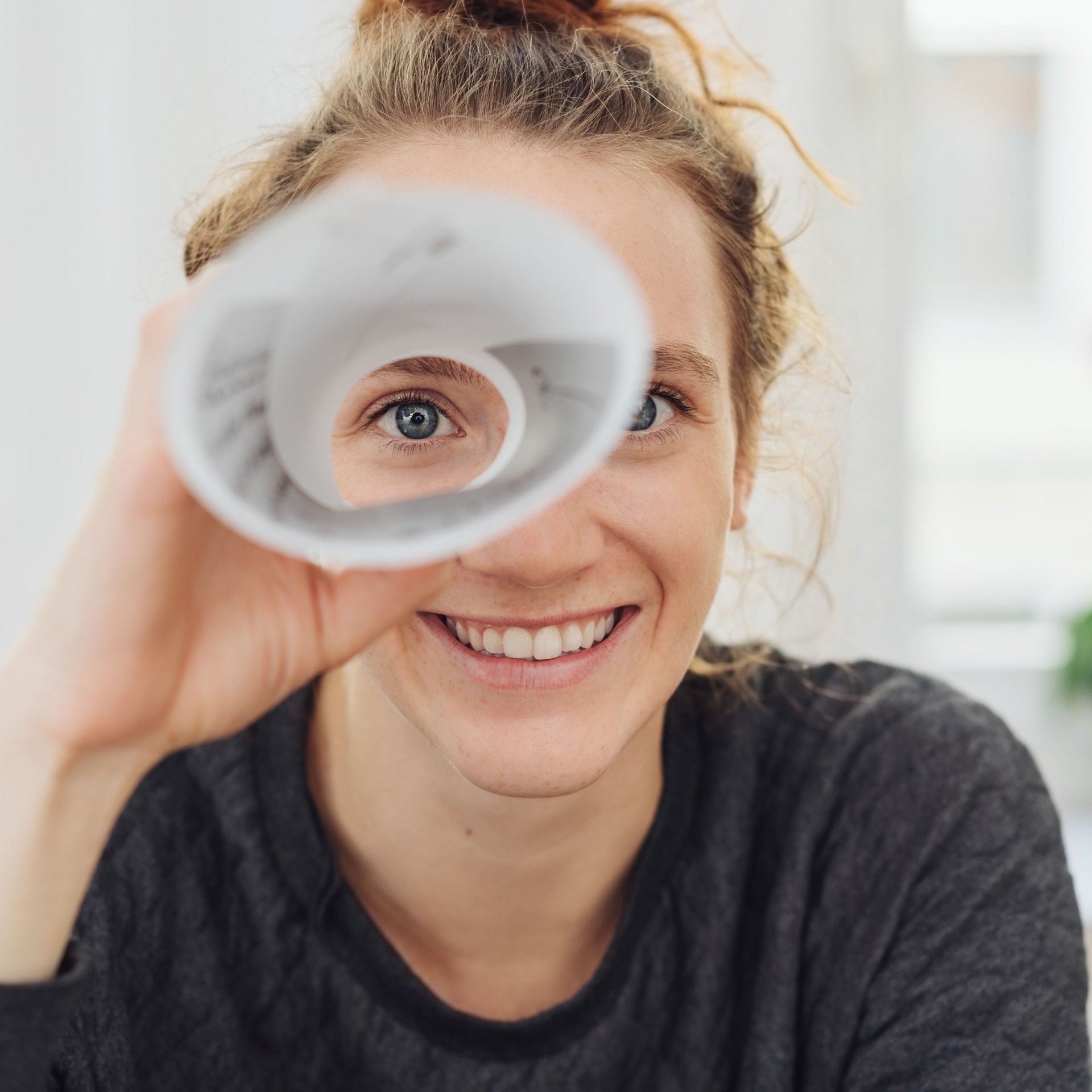 Eine junge Frau schaut durch ein Fernrohr aus Papier und lacht dabei.
