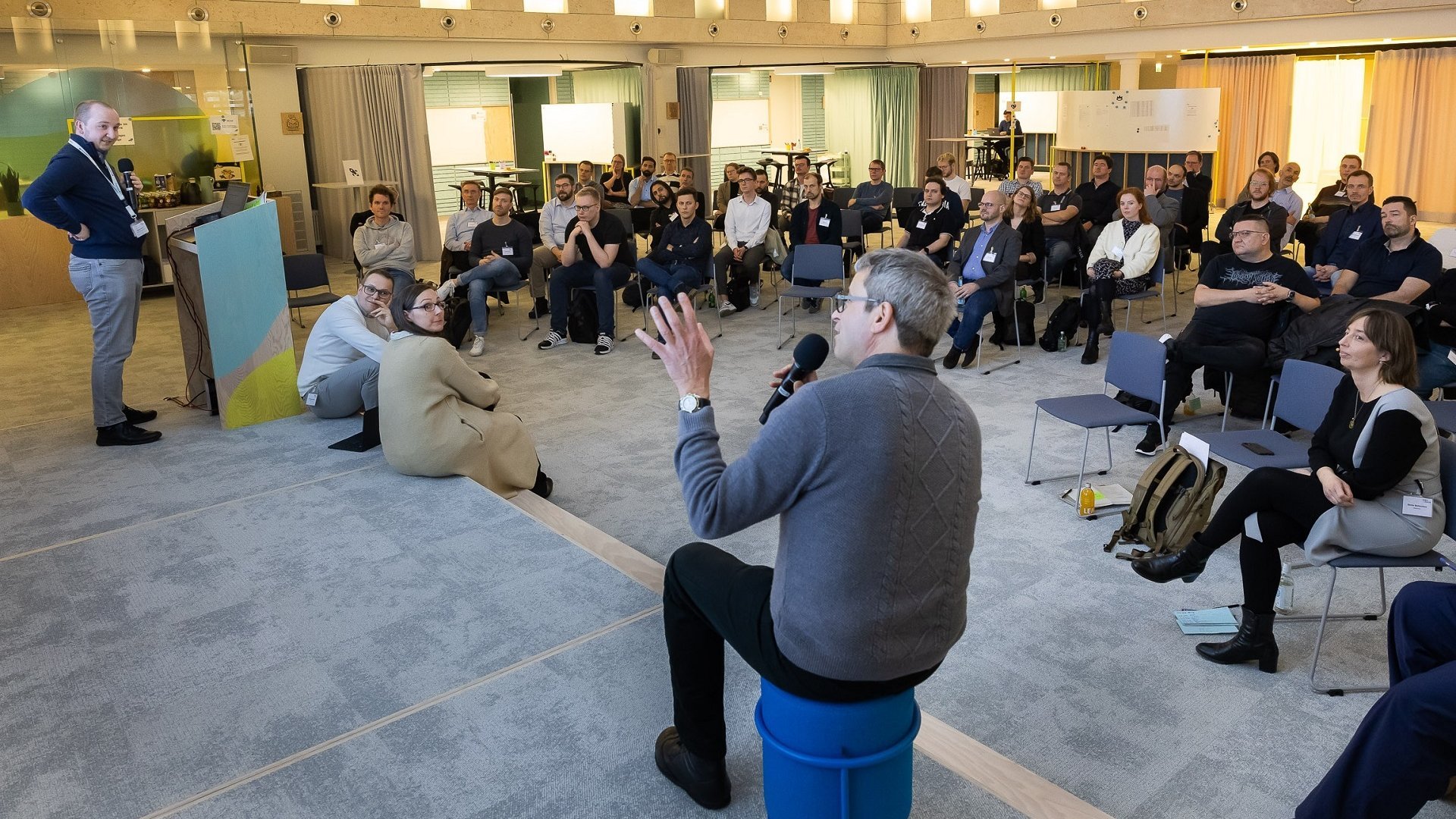 [Translate to English:] Ein Mann mit Mikrofon in der Mitte eines Podiums umgeben von Zuhörern bei einer Diskussion im Rahmen des Stakeholder-Prozesses zur Entwicklung der digitalen Vernetzungsinfrastruktur.