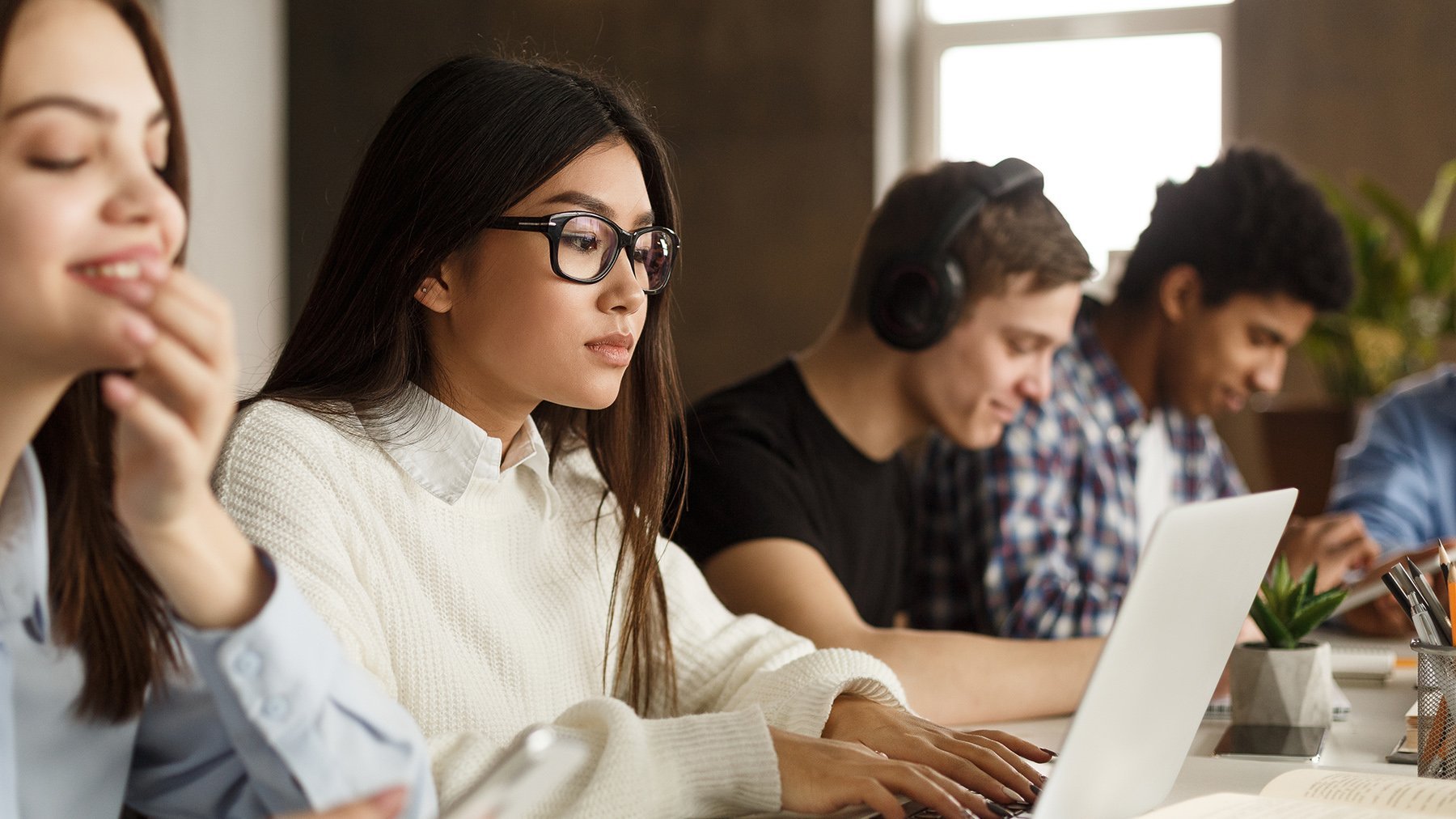 Das Bild zeigt eine Gruppe von Studenten, die Laptop und Mobiltelefone benutzen, während sie zusammen lernen