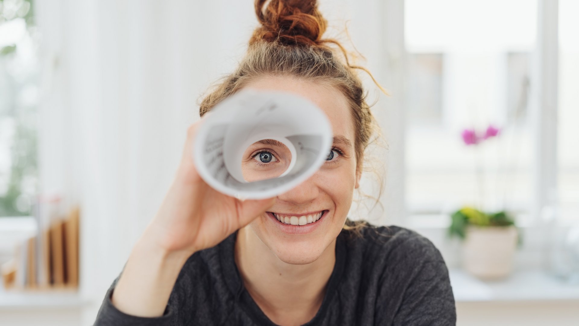 Eine Frau guckt durch ein gerolltes Blatt.