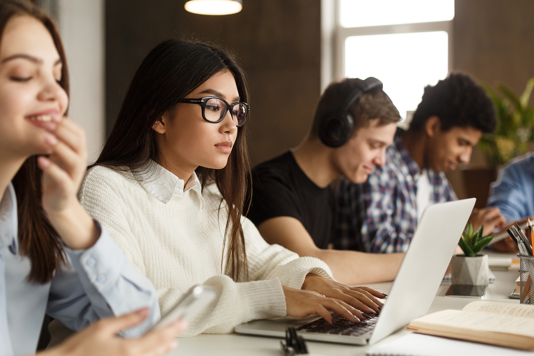 Das Bild zeigt eine Gruppe von Studenten, die Laptop und Mobiltelefone benutzen, während sie zusammen lernen