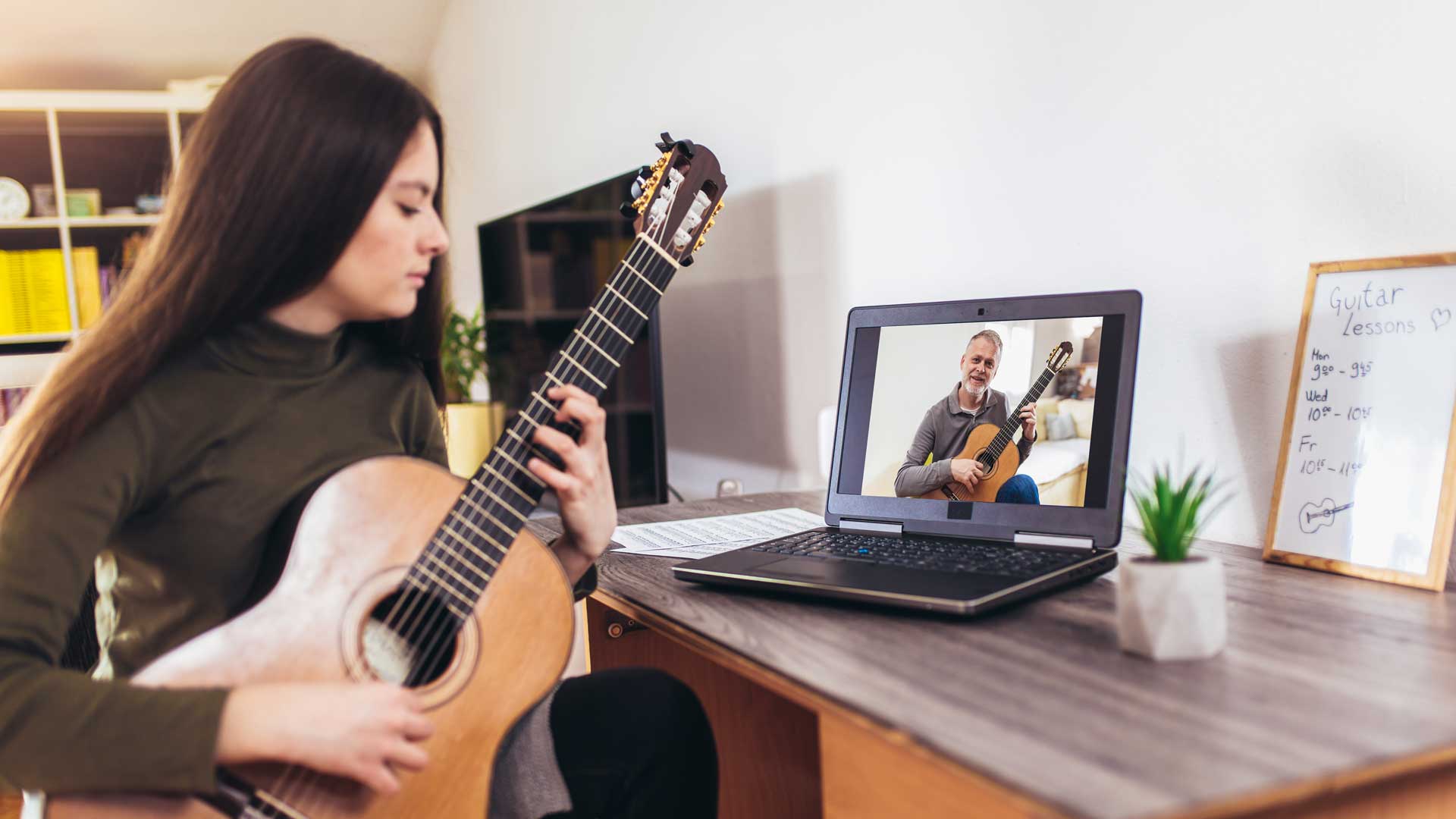 Ein wird online vor Ihrem Laptop an der Gitarre unterrichtet.