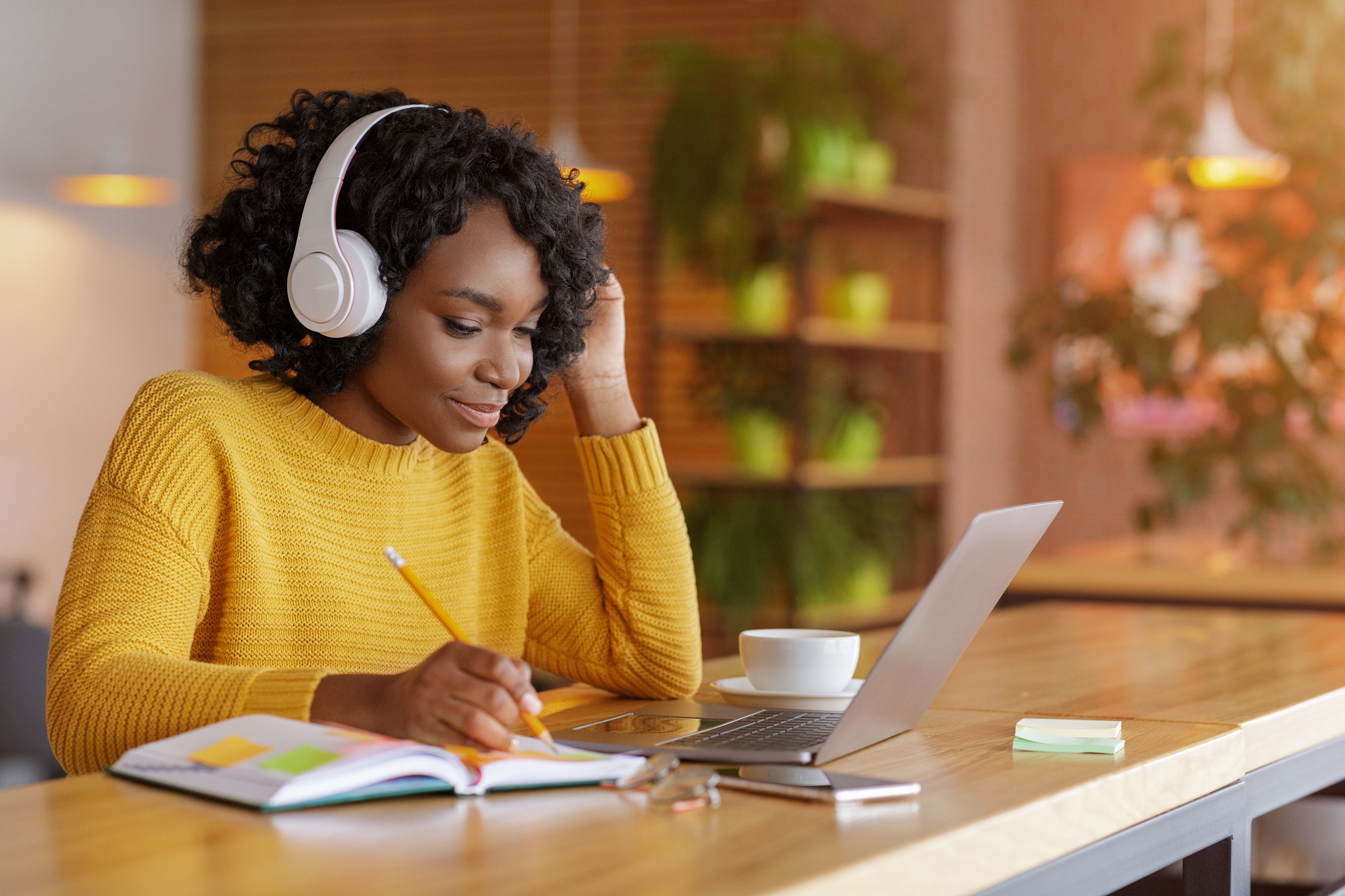 Das Bild zeigt ein Mädchen mit Kopfhörern, das Notizen macht und am Laptop arbeitet 